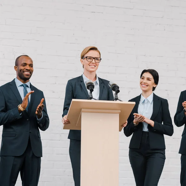 Happy multicultural businessmen and businesswoman applauding to attractive speaker — Stock Photo