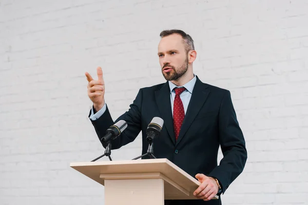 Schöner bärtiger Redner gestikuliert, während er in der Nähe von Mikrofonen spricht — Stockfoto