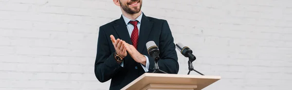 Panoramaaufnahme eines glücklichen bärtigen Redners, der an Mikrofonen applaudiert — Stockfoto