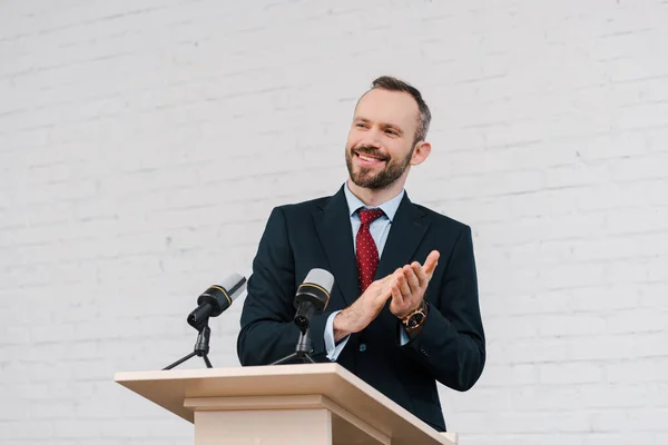 Heureux haut-parleur barbu applaudissant près des microphones — Photo de stock