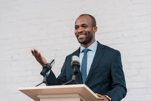 Heureux orateur afro-américain gesticulant près des microphones — Photo de stock