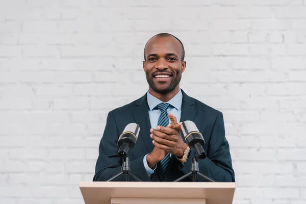 Happy african american speaker applauding near microphones — Stock Photo