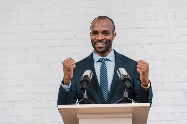 Happy african american speaker standing with clenched fists near microphones — Stock Photo