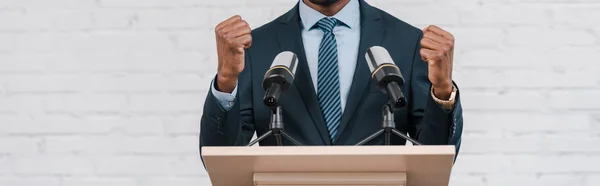 Panoramic shot of african american speaker standing with clenched fists near microphones — Stock Photo