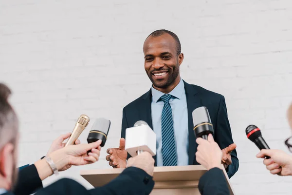 Cropped view of journalists holding microphones near happy african american diplomat — Stock Photo