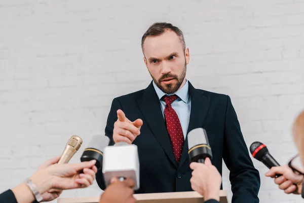 Ausgeschnittene Ansicht von Journalisten, die Mikrofone in der Nähe eines bärtigen Diplomaten halten, der mit dem Finger zeigt — Stockfoto