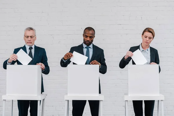 Votantes multiculturales que ponen boletas en las urnas - foto de stock