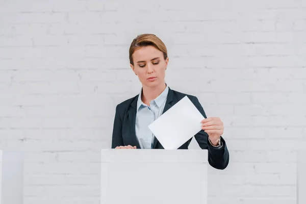 Attractive businesswoman voting near brick wall — Stock Photo