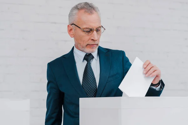 Bearded businessman in glasses voting near brick wall — Stock Photo