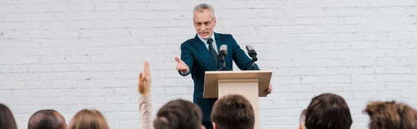 Panoramaaufnahme eines glücklichen Redners, der mit erhobener Hand auf Journalisten zeigt — Stockfoto