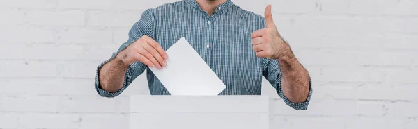 Prise de vue panoramique de l'électeur montrant le pouce levé tout en tenant un bulletin de vote blanc — Photo de stock