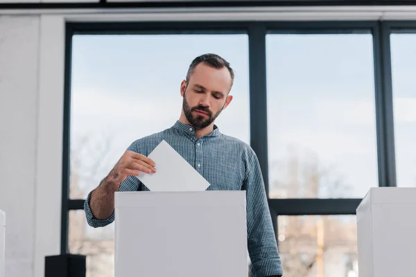 Bärtiger und gutaussehender Bürger wirft leere Stimmzettel in die Wahlurne — Stockfoto