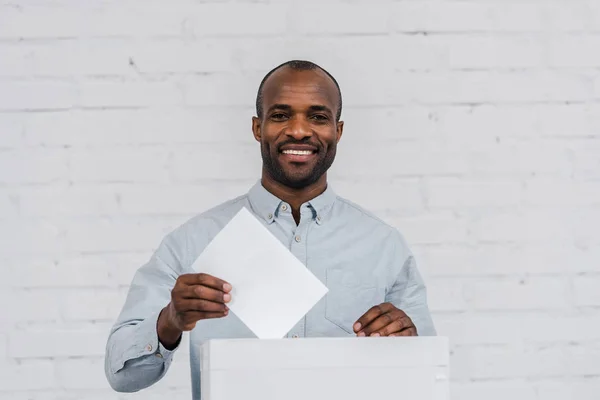 Happy african american voter putting blank ballot in voting box — Stock Photo