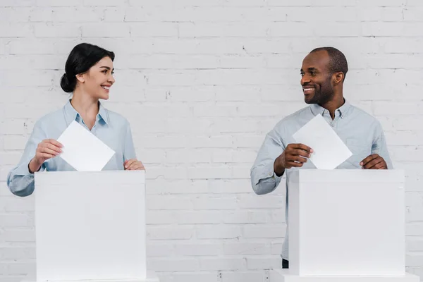 Happy woman and african american man voting near brick wall — Stock Photo