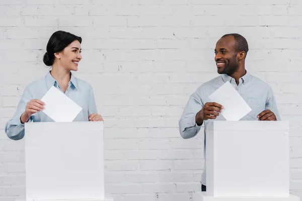 Mujer feliz y hombre afroamericano votando cerca de la pared de ladrillo - foto de stock