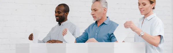 Panoramic shot of happy multicultural citizens voting while standing near boxes — Stock Photo