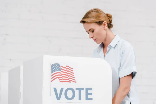 Приваблива жінка, що голосує біля підставки з написанням голосів та американським прапором — стокове фото