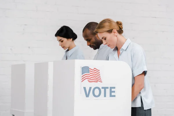 Side view of women and african american man voting near vote lettering and brick wall — Stock Photo