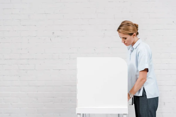 Beautiful woman voting near stand and brick wall — Stock Photo