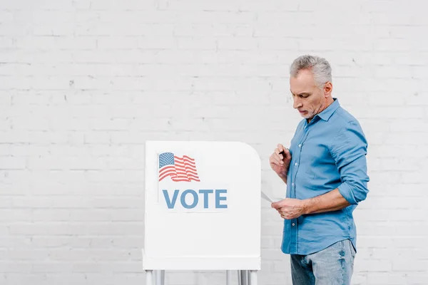 Bürger hält Stift in der Hand, während er Wahlzettel in der Nähe des Wahlstandes betrachtet — Stockfoto