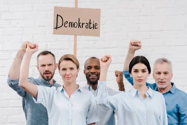 Grupo de personas multiculturales haciendo gestos cerca de pancarta con letras demokratie - foto de stock