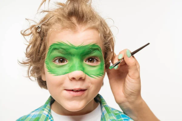 Visão recortada do artista pintando máscara de gecko no rosto de menino desgrenhado e alegre isolado no branco — Fotografia de Stock