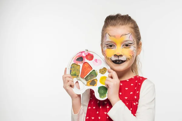 Smiling child with tiger muzzle painting on face showing palette isolated on white — Stock Photo