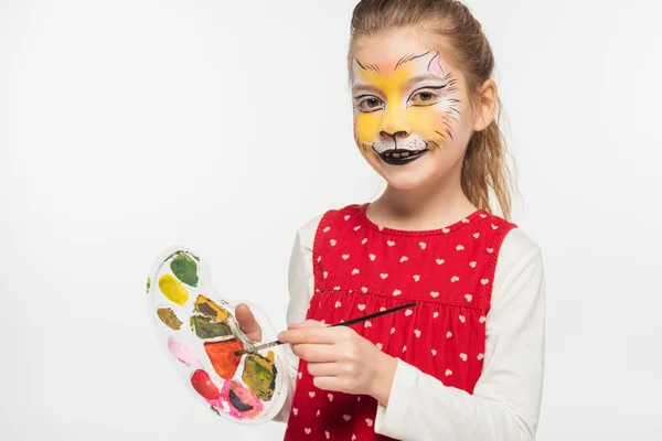Cute child with tiger muzzle painting on face holding palette and paintbrush while looking at camera isolated on white — Stock Photo