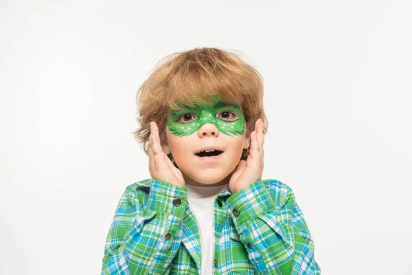 Niño sorprendido con máscara de geco pintado en la cara de la mano cerca de la cara mientras mira la cámara aislada en blanco - foto de stock