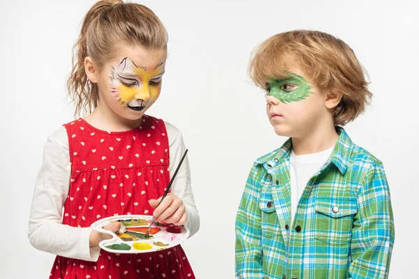 Adorabile bambino con gatto museruola viso pittura tenendo tavolozza e pennello vicino ragazzo con dipinto maschera di geco isolato su bianco — Foto stock