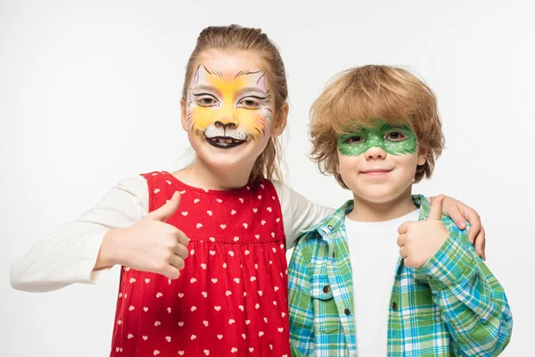 Cheerful friends with cat muzzle and gecko mask paintings on faces showing thumbs up isolated on white — Stock Photo