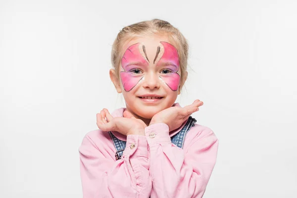 Lächelndes Kind mit Schmetterlingsmalerei im Gesicht, die Hände vor dem Gesicht haltend, während es isoliert auf weiß in die Kamera schaut — Stockfoto