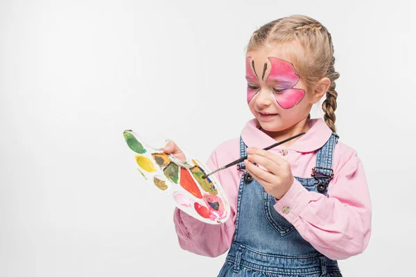 Entzückendes Kind mit Schmetterlingsmalerei im Gesicht mit Palette und Pinsel isoliert auf weiß — Stockfoto