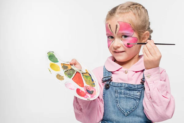 Улыбающийся ребенок с бабочкой живописи на лице держа палитру и кисть, изолированные на белом — стоковое фото