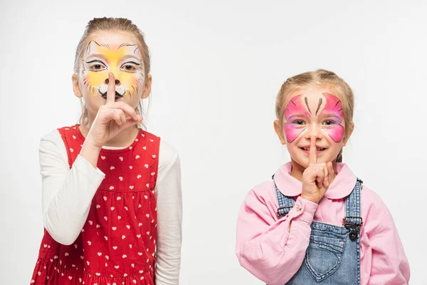 Adorables amigos con bozal de gato y pinturas de mariposas en caras que muestran un signo de silencio aislado en blanco - foto de stock