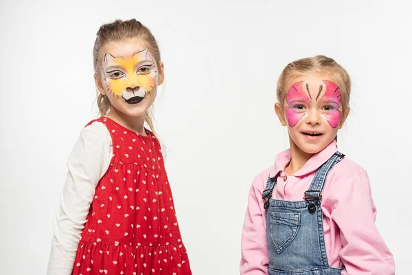 Adorable children with cat muzzle and butterfly paintings on faces looking at camera isolated on white — Stock Photo