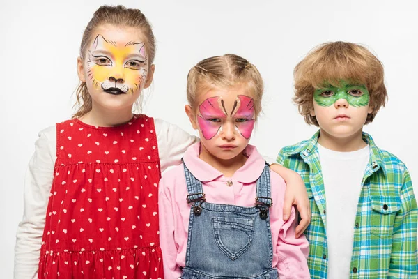 Displeased friends with colorful face paintings looking at camera isolated on white — Stock Photo