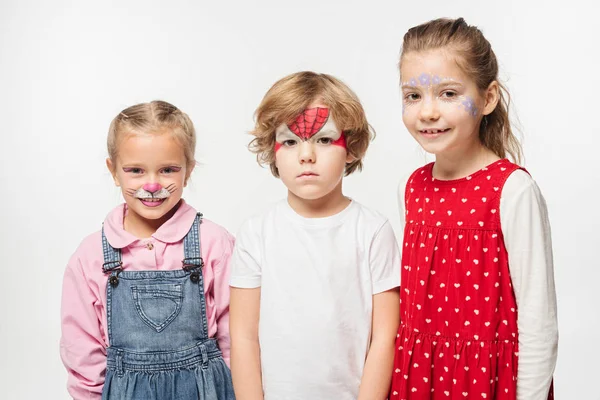 Fröhliche Kinder und beleidigte Jungen mit bunten Gesichtsbemalungen, die isoliert auf weiß in die Kamera schauen — Stockfoto