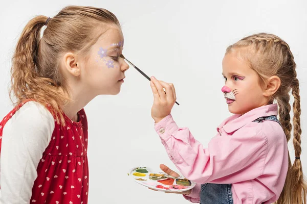 Mignon enfant avec peint chat muselière peinture motif floral sur le visage d'un ami isolé sur blanc — Photo de stock