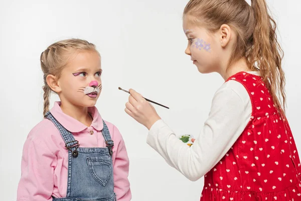 Mignon enfant avec motif floral sur le visage tenant pinceau ami proche avec muselière peinte chat isolé sur blanc — Photo de stock