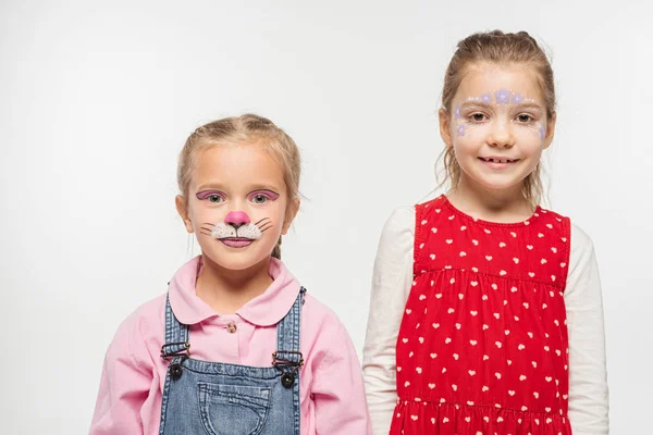 Adorable niños con flores y gato bozal pinturas en caras sonriendo a cámara aislada en blanco - foto de stock