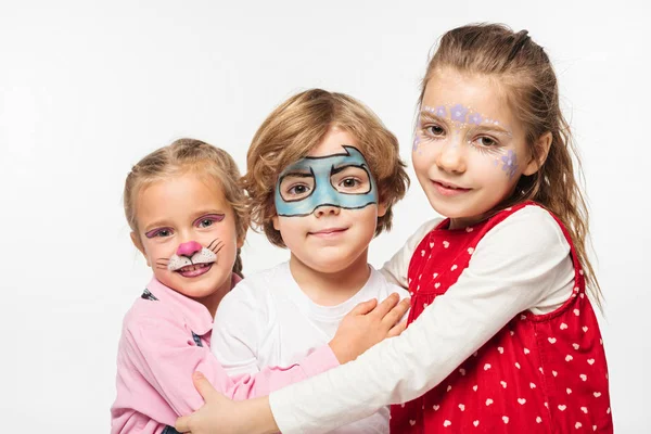 Amigos felizes com pinturas faciais coloridas abraçando enquanto olha para a câmera isolada no branco — Fotografia de Stock