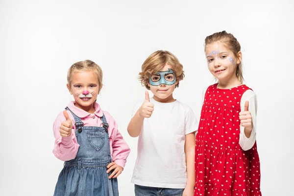 Amigos alegres con coloridas pinturas faciales que muestran los pulgares hacia arriba mientras mira la cámara aislada en blanco - foto de stock