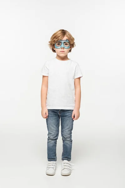 Full length view of adorable boy with superhero mask painted on face looking at camera on white background — Stock Photo