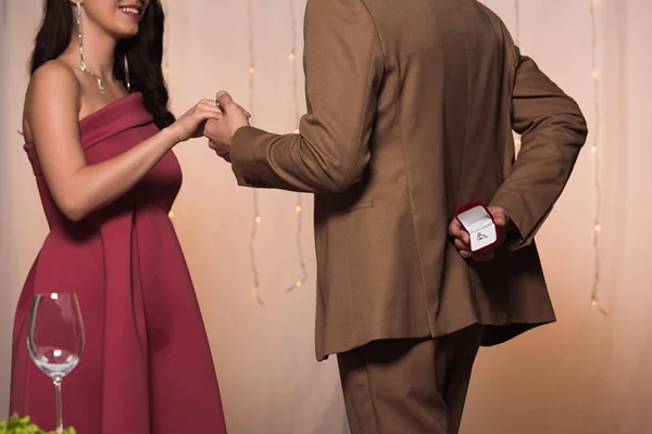 Vue recadrée de l'homme élégant tenant la main de petite amie heureuse tout en faisant la demande en mariage — Photo de stock