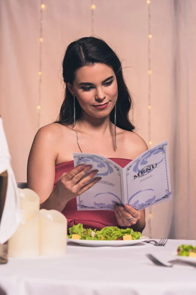 Atraente, elegante menu de leitura menina enquanto sentado no restaurante — Fotografia de Stock