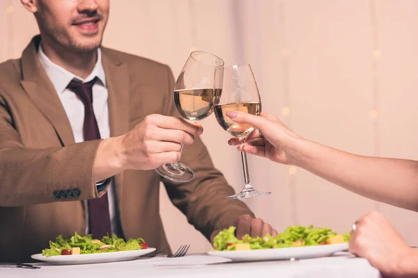 Vista recortada de hombre tintineo vasos de vino blanco con novia mientras está sentado en el restaurante - foto de stock
