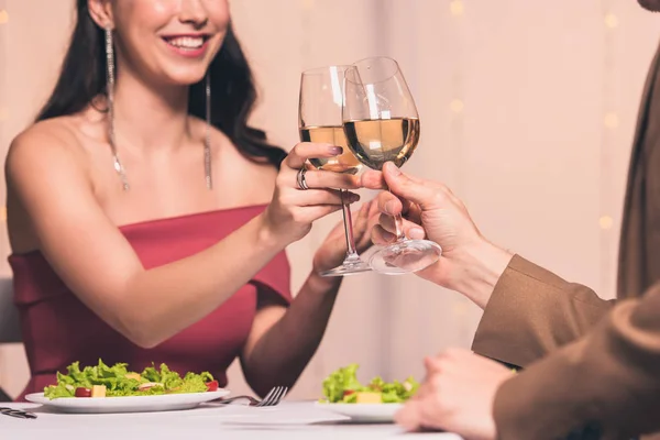 Cropped view of woman clinking glasses of white wine with boyfriend while sitting in restaurant — Stock Photo