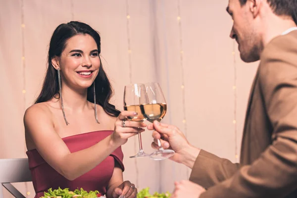 Feliz, elegante hombre y mujer tintineo vasos de vino blanco mientras está sentado en el restaurante - foto de stock