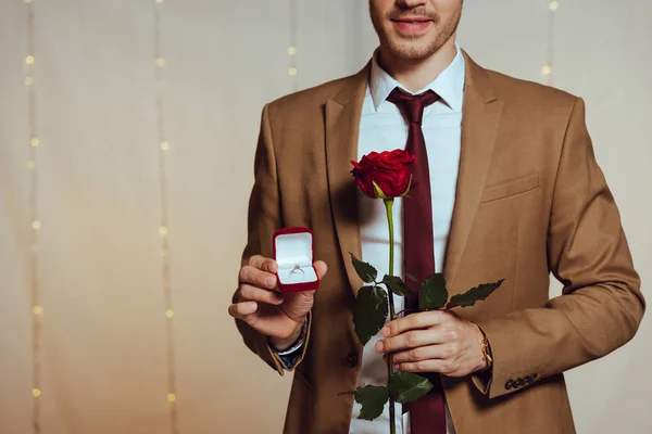 Partial view of elegant man holding box with wedding ring and red rose while standing in restaurant — Stock Photo